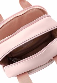 Liten rosa ryggsäck gjord av syntetiskt material med en slät yta, dubbel dragkedja och en foder inuti. Har två justerbara axelremmar.