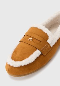 Brown suede slipper with a white faux fur lining, featuring a decorative strap and subtle hardware accents on the upper. Rounded toe design.