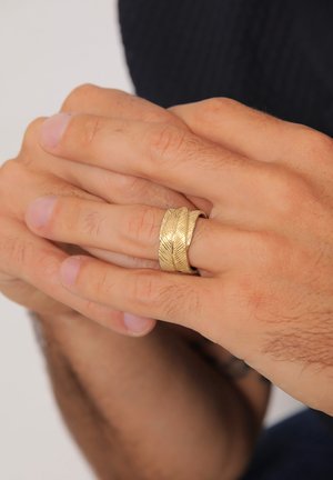 Anello in oro con un motivo a foglia testurizzato, caratterizzato da un interno liscio e una fascia ampia, indossato su una mano con un tono di pelle chiaro.