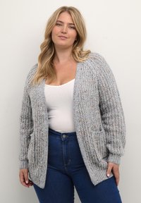 Light gray knitted cardigan with an open front, ribbed texture, and two front pockets, worn over a white top and blue jeans.