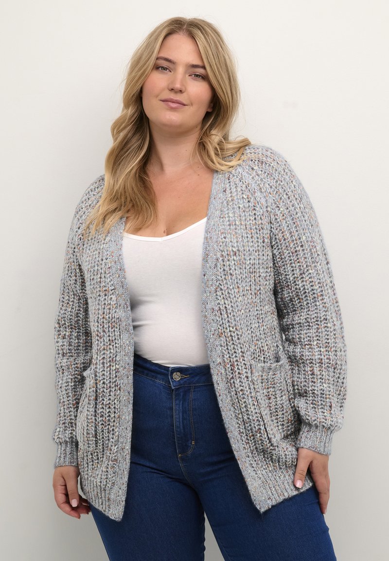 Light gray knitted cardigan with an open front, ribbed texture, and two front pockets, worn over a white top and blue jeans.