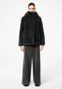 Cappotto in pelliccia sintetica grigio scuro con colletto alto, chiusura frontale e tasche laterali, abbinato a pantaloni grigi a gamba larga. Texture liscia, design squadrato.