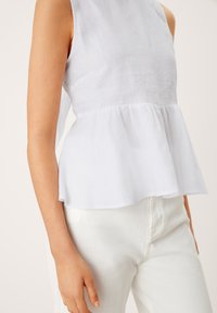 Top peplum bianco in lino con design senza maniche. Il tessuto è leggero e leggermente testurizzato. Abbinato a pantaloni in denim bianchi.