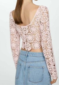 Top de encaje rosa con mangas largas, patrón floral, espalda baja y un dobladillo con forma de onda, combinado con una falda de mezclilla azul clara con bolsillos traseros.