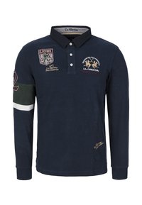 Granatowa koszulka polo z długim rękawem, z haftowanymi naszywkami, kołnierzykiem i listwą z guzikami. Posiada zielone i białe akcenty na rękawach i na dole.