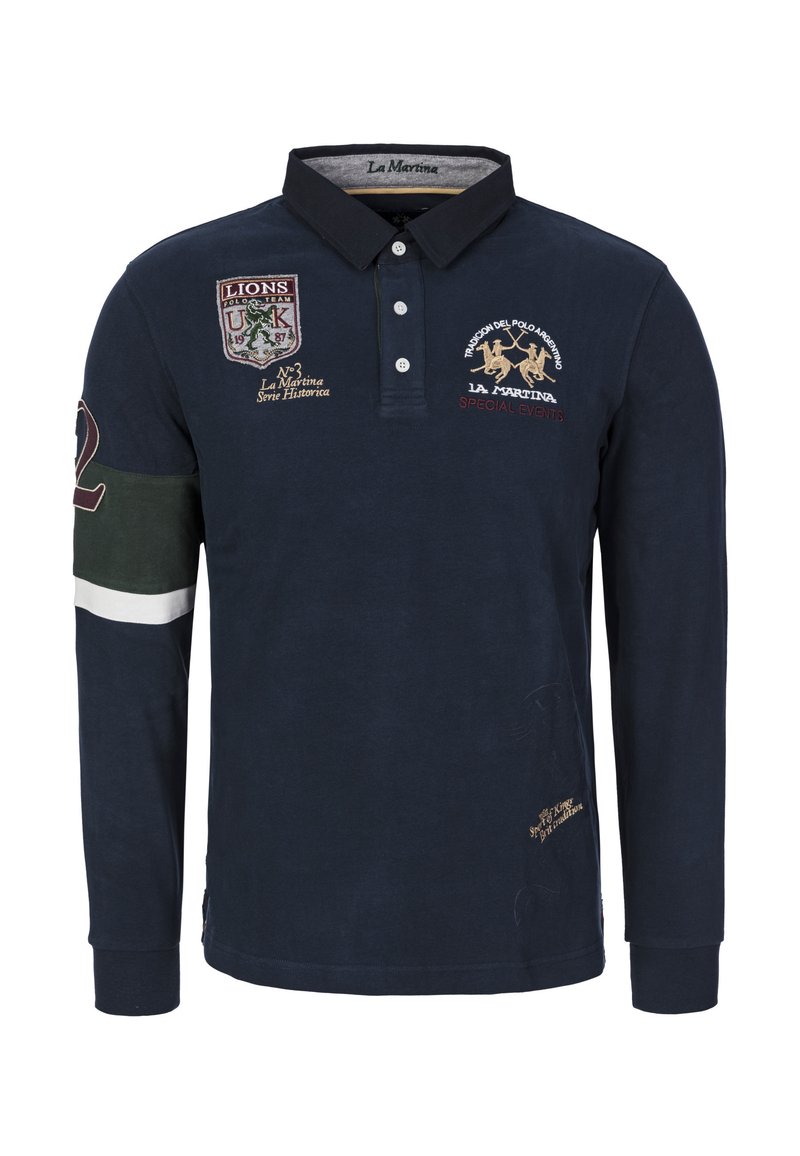 Granatowa koszulka polo z długim rękawem, z haftowanymi naszywkami, kołnierzykiem i listwą z guzikami. Posiada zielone i białe akcenty na rękawach i na dole.