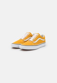 Gule sued sneakers med en hvit aksentstripe, hvite snøringer og svart trim rundt sålen. Klassisk lav-topp design.