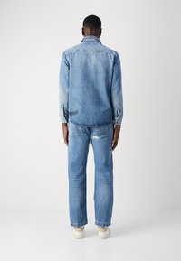 Chaqueta de mezclilla azul claro con cuello y puños abotonados, combinada con jeans azul claro a juego. Ambas prendas presentan un aspecto ligeramente desgastado.