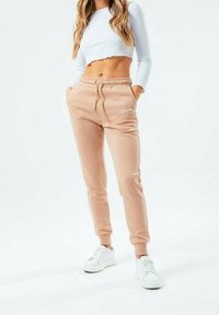 Světlé béžové jogger kalhoty s elastickým pasem a bočními kapsami, zdobené bílým vyšitým textem. Kombinované s bíým zkráceným topem s žebrovanou strukturou.