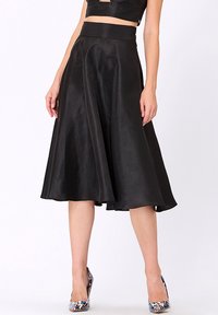 Jupe en satin noir en A avec une taille haute, texture lisse, longueur genou, associée à des chaussures à talons hauts à motifs multicolores.