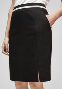 Černá tužková sukně s přiléhavým střihem, s kontrastním tenkým šedým pruhem v pase a s bočním rozparkem. Hladká látka s kapsami.