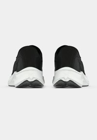 Paire de chaussures de sport noires avec tissu texturé et semelles blanches épaisses, vues de dos sur fond blanc.