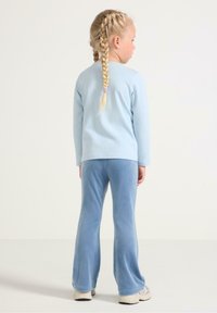 Chemise à manches longues bleu clair associée à un pantalon de jogging évasé bleu doux, tous deux en tissu pelucheux. Chaussures de sport de couleur claire.