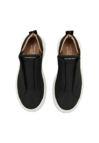 Sneakers neri slip-on con una superficie liscia, dotati di pannelli elastici, suola in gomma bianca e soletta beige con dettagli di branding minimi.