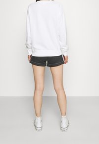 Witte oversized sweatshirt met lange mouwen en geribbelde manchetten, gecombineerd met grijze spijkershorts. Draagt witte hoge sneakers.