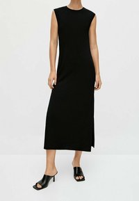 Abito midi senza maniche nero con taglio dritto e spacco laterale, realizzato in tessuto a coste; abbinato a mule nere open-toe.