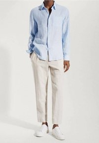 Camisa de lino azul claro de manga larga con un bolsillo en el pecho, combinada con pantalones de lino beige claros y zapatillas blancas. Diseño sencillo y ajustado.