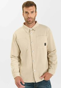 Beige corduroy jas met een gekraagde nek, twee borstzakken, drukkknopen en lange mouwen, met een textuurpatroon.