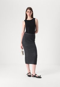 Svart ribbet tanktop med sølvnagler, grå midikjole med vertikal tekstur, og svarte slingback-lettelser med sløyfedetalj. Liten hvit håndveske.