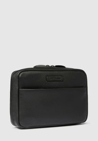 Zwarte leren tas met een getextureerd oppervlak, ritssluiting, voorvak en merklabel. Compacte rechthoekige vorm.