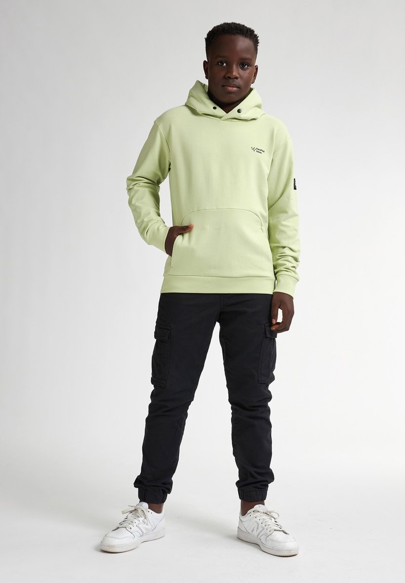Felpa verde chiaro con tasca frontale e cappuccio con cordini, abbinata a pantaloni cargo neri a gamba affusolata e sneaker bianche.