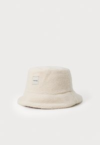 Klobouk s širokým okrajem vyrobený z měkkého krémového materiálu. Má texturovaný povrch a malou etiketou Calvin Klein po straně.