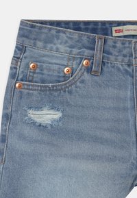 Ljusblå denimjeans med en slitna ficka med fransiga kanter, kopparfärgade detaljer och kontrasterande orange sömmar.