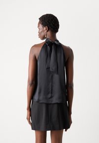 Čierny saténový halter top s mašľou vzadu, s hladkou textúrou a voľným strihom. Spárovaný s čiernou sukňou.