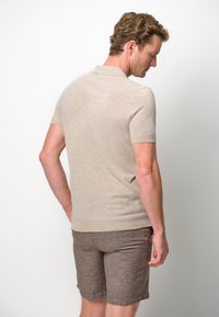 Beige short-sleeve polo in soft knit material, featuring a classic collar and fitted design, paired with brown linen shorts.