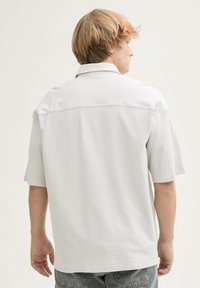 Korte mouwen, lichtgrijze polo met een gestructureerde stof, relaxte pasvorm en een rugpaneel naaddetail. Casual ontwerp, geschikt voor warm weer.