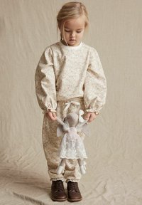 Krämfärgad loungewear-set i blommönster med pastellfärger, med rynkade ärmar och elastiska manschetter. Barnet håller en tygdocka.
