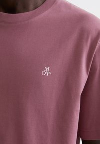 Camiseta de manga corta en color rosa suave, hecha de algodón suave. Presenta un pequeño logo blanco "MOP" en la parte izquierda del pecho. Textura suave.