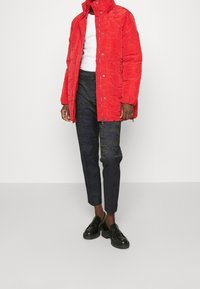 Rode gewatteerde pufferjack met een hoge kraag, gecombineerd met donkere, gemusterde broek en zwarte instappers, met een slanke, op maat gemaakte pasvorm.