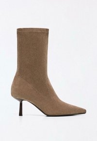 Cizmă medie din piele întoarsă taupe, cu vârf ascuțit și toc subțire tip kitten, stivuită, pe fundal alb.