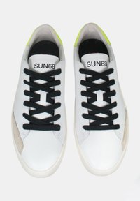 Sneaker bianche con lacci neri, con un accento in suede beige sul lato e un colletto verde neon. Branding visibile sulla linguetta.