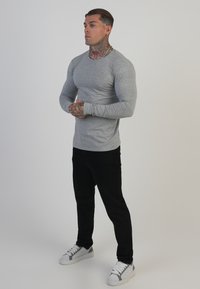 Camisa gris de manga larga ajustada con cuello redondo, combinada con pantalones negros de corte slim y zapatillas blancas con detalles grises.