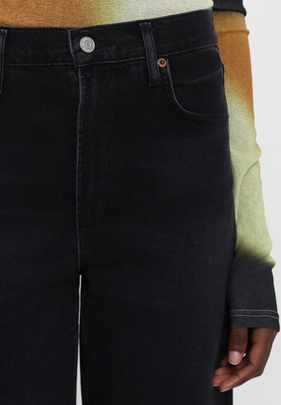 High-waisted black denim jeans with a structured shape, subtle fading, silver button closure, and classic five-pocket design.