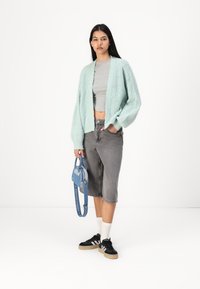 Myntgrön stickad kofta, grå st cropped topp, grå denim Bermudashorts, svarta sneakers med vita ränder och en blå handväska.