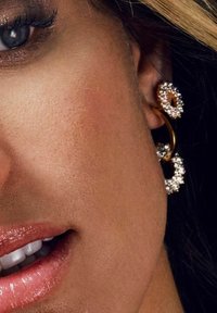 Boucles d'oreilles en or en forme de cercle avec des strass étincelants, présentant une surface texturée et une finition brillante.