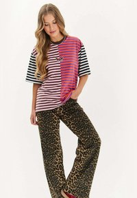 Paskowana, oversize t-shirt w kolorach różowym, pomarańczowym i czarnym; szerokie spodnie w panterkę. Haft motyla na lewej stronie klatki piersiowej koszulki.