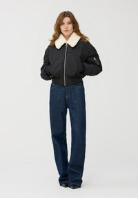 Czarna bomberka z białym futrzanym kołnierzem, z zamkiem błyskawicznym i bocznymi kieszeniami. Połączona z luźnymi niebieskimi dżinsami.
