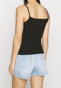 Czarny top bez rękawów z cienkimi ramiączkami, dopasowany krój, zestawiony z jasnoniebieskimi dżinsowymi szortami z postrzępionymi brzegami i tylnymi kieszeniami.