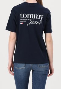Námořnická modrá bavlněná tričko s bílým textem na zadní straně: "tommy Jeans," "New York City, NY," a "Od roku 1985," s akcentem loga.