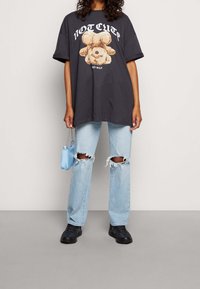 T-shirt grigia oversize con una grafica di un orsetto e il testo "NON CARINO", abbinata a jeans chiari strappati e sneakers nere.