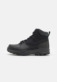 Svart mid-top støvler med en kombinasjon av glatt lær og strukturert stoff, med metalløyelets, en robust såle og en bakre pull-tab.
