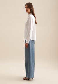 Chemise blanche en lin à manches longues avec un col, associée à une jupe en denim taille haute. Talons aiguilles noirs ouverts à l'avant et accessoires minimalistes.