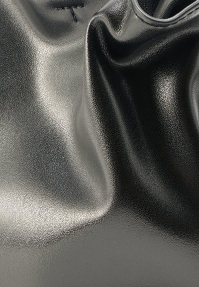 Μαύρο γυαλιστερό δέρμα με ορατή λεπτή υφή και φυσικές πτυχώσεις που δημιουργούν αντανακλάσεις φωτός και σκιές.
