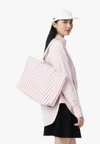 Bolso de lona con franjas verticales en rosa y blanco, que presenta dos asas resistentes, un interior espacioso y elementos de diseño minimalistas.