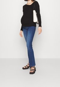 Musta pitkähihainen paita, slim fit -siniset farkut ja mustat hihnasaappaat. Asusteina pieni valkoinen käsilaukku mustalla hihnalla.