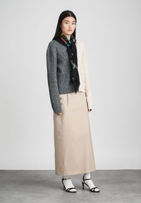 Γκρι και κρέμ πλεχτό πουλόβερ, μπεζ μάξι φούστα, μαύρο κασκόλ με σχέδιο, λευκές κάλτσες και μαύρες ψηλοτάκουνες σαγιονάρες. Λείες υφές, ξεχωριστά χρώματα.